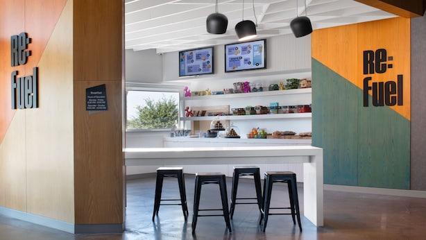 A modern kitchen with a central island, bar stools, and a breakfast sign indicating hours of operation. - Aloft by Marriott McAllen (McAllen)