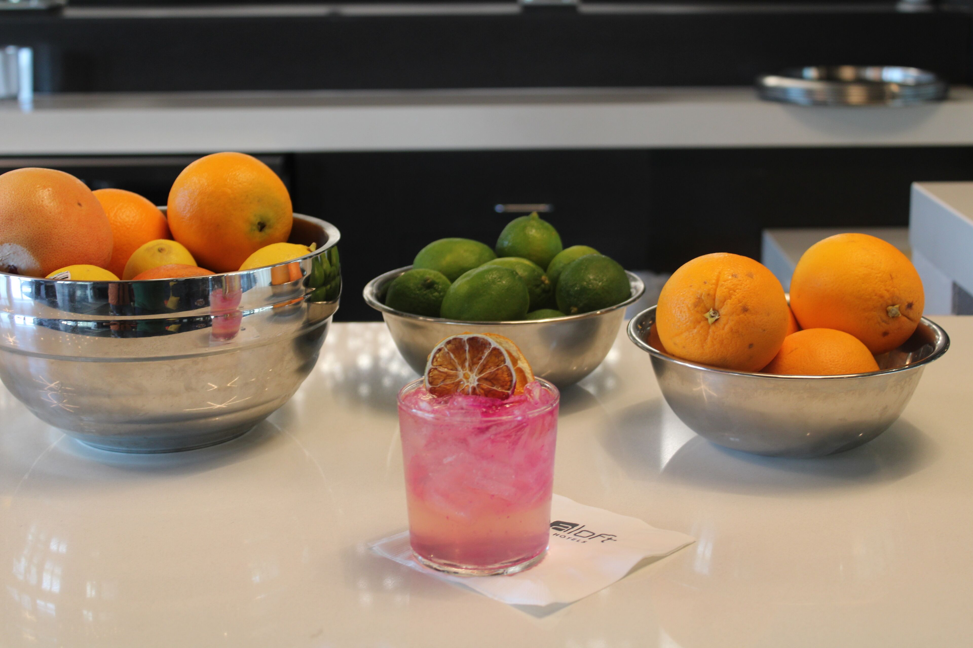 A kitchen counter with three metal bowls containing oranges and limes.