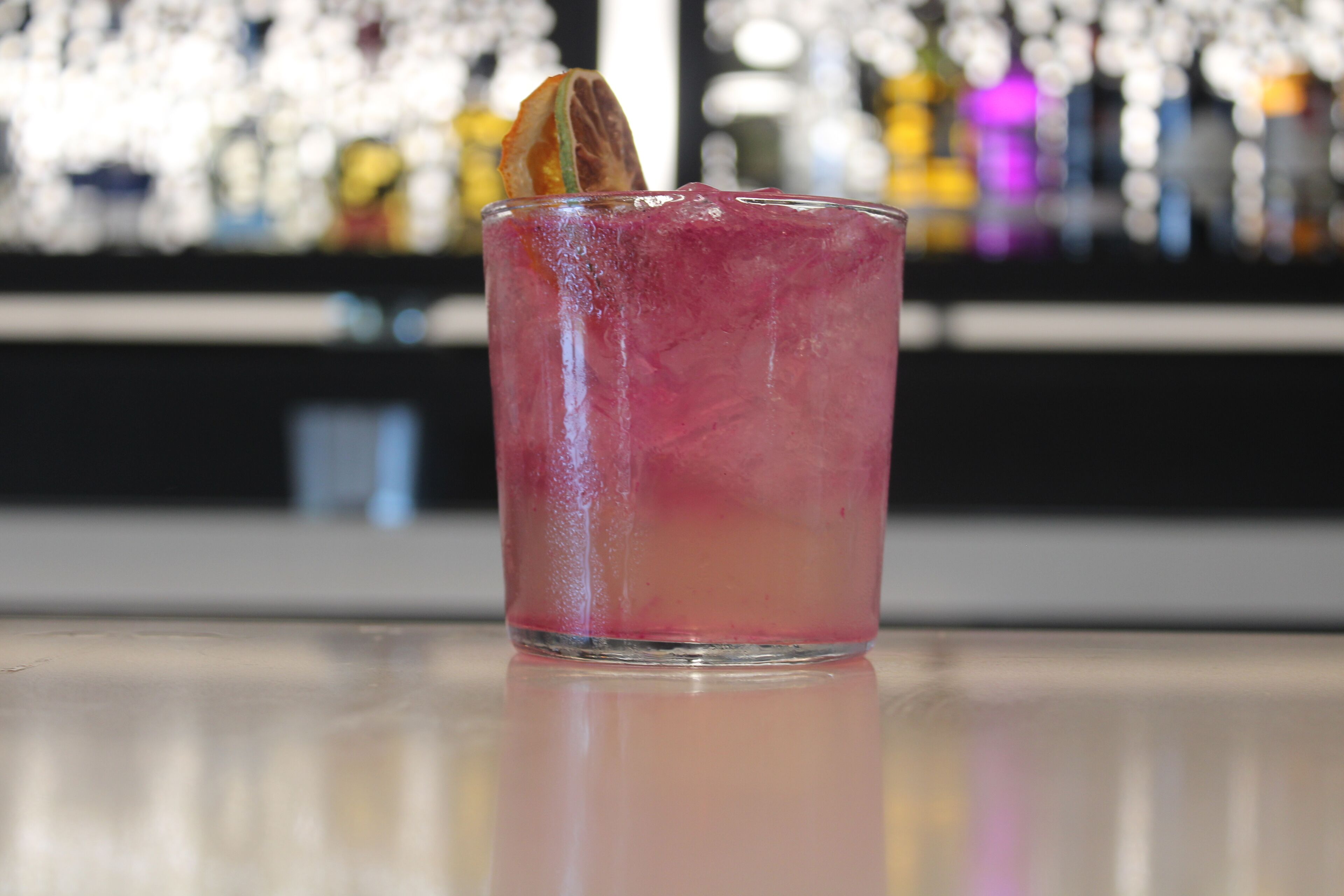 A glass of pink beverage with a garnish on a bar counter.