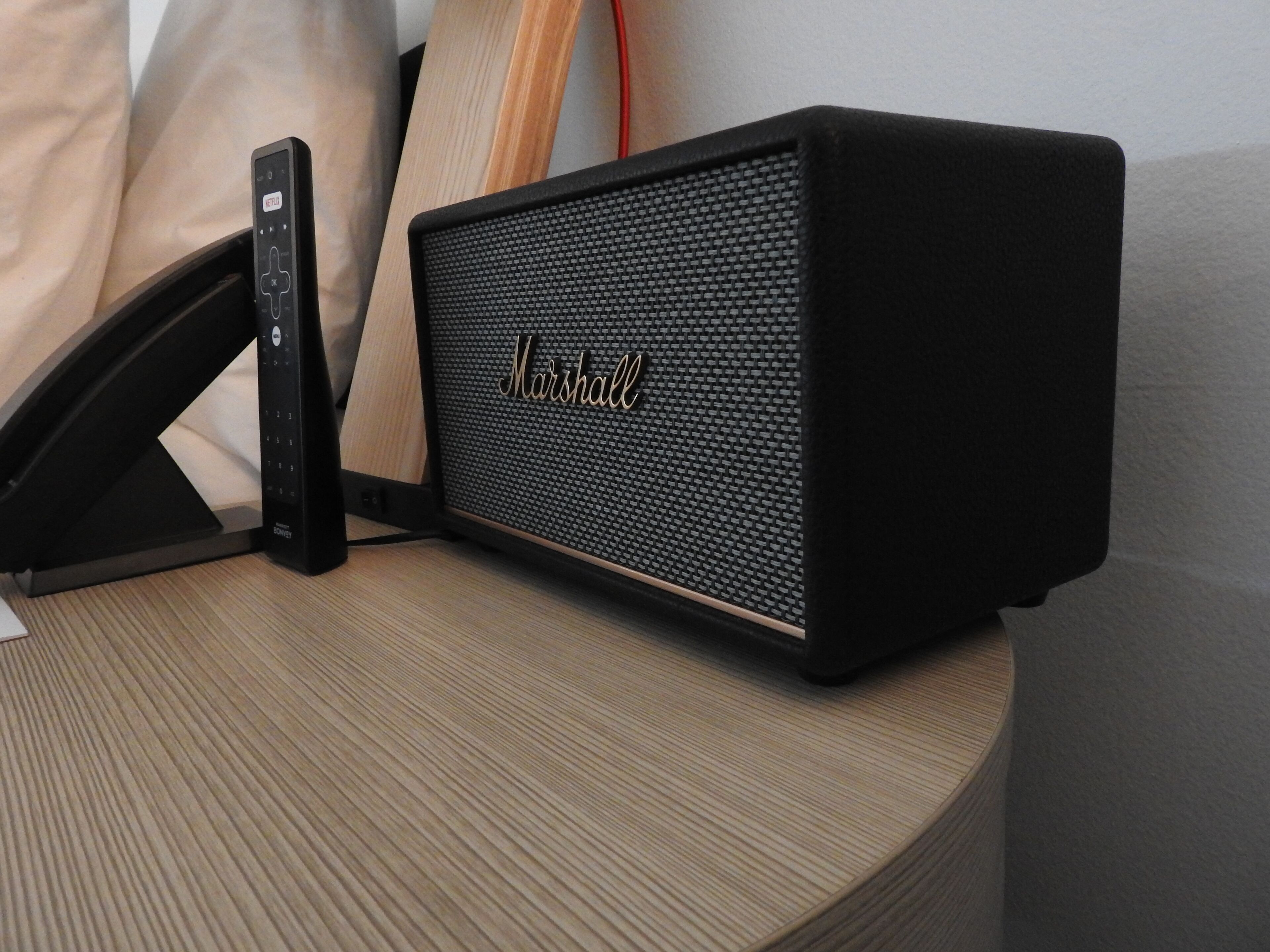 A black Marshall speaker on a wooden table with a remote control.