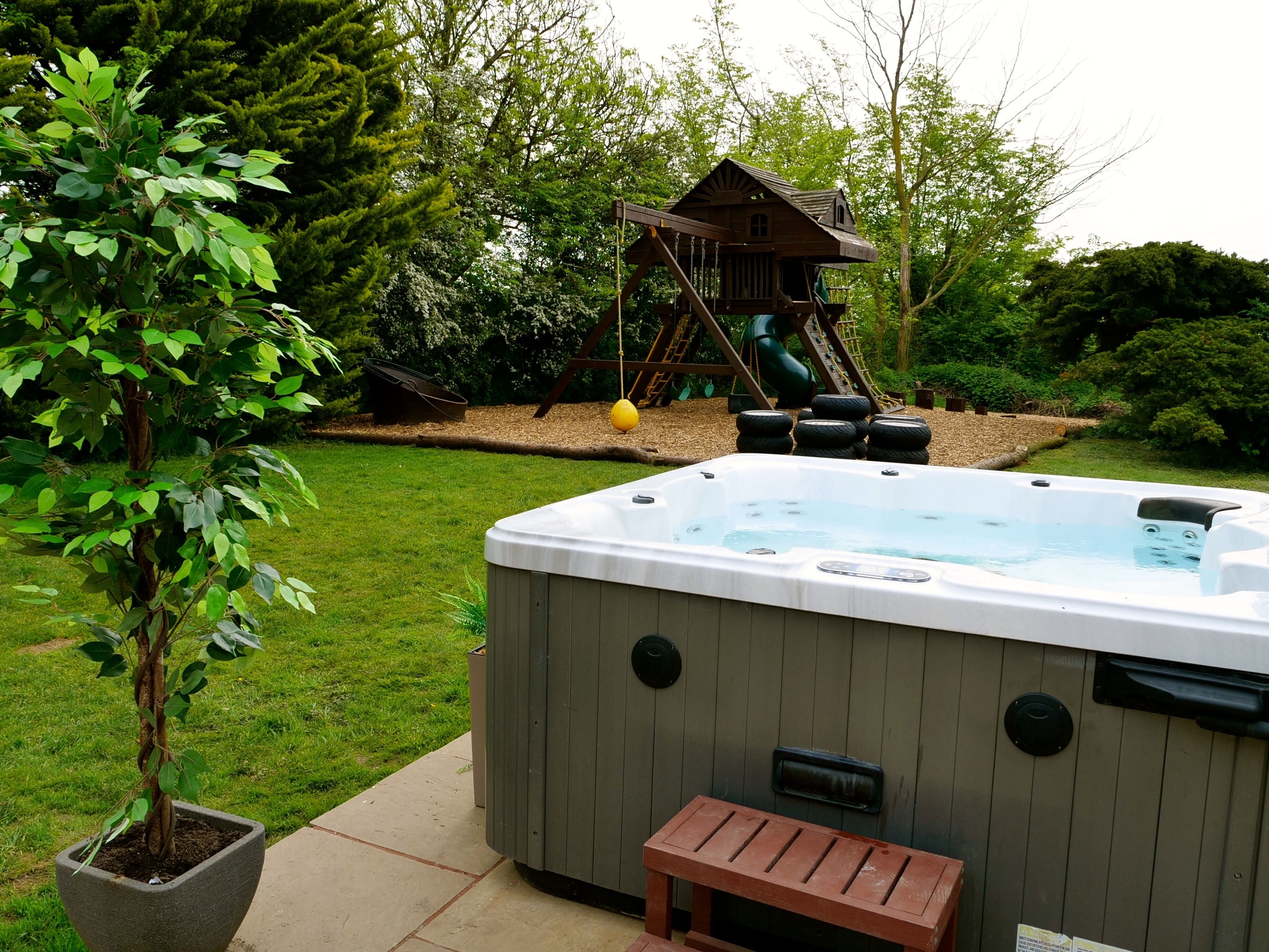 Un jacuzzi dans un jardin, avec une cabane en bois et un arbre.