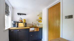 Une cuisine compacte avec des meubles de couleur sombre, un plan de travail en bois, une bouilloire, une machine à café et un évier.