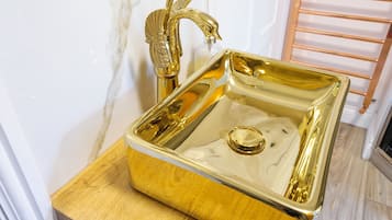 A gold bathroom sink with a decorative faucet and a wooden base.
