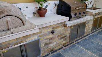 An outdoor kitchen with a stone wall, a pizza oven, a grill, and a sink.