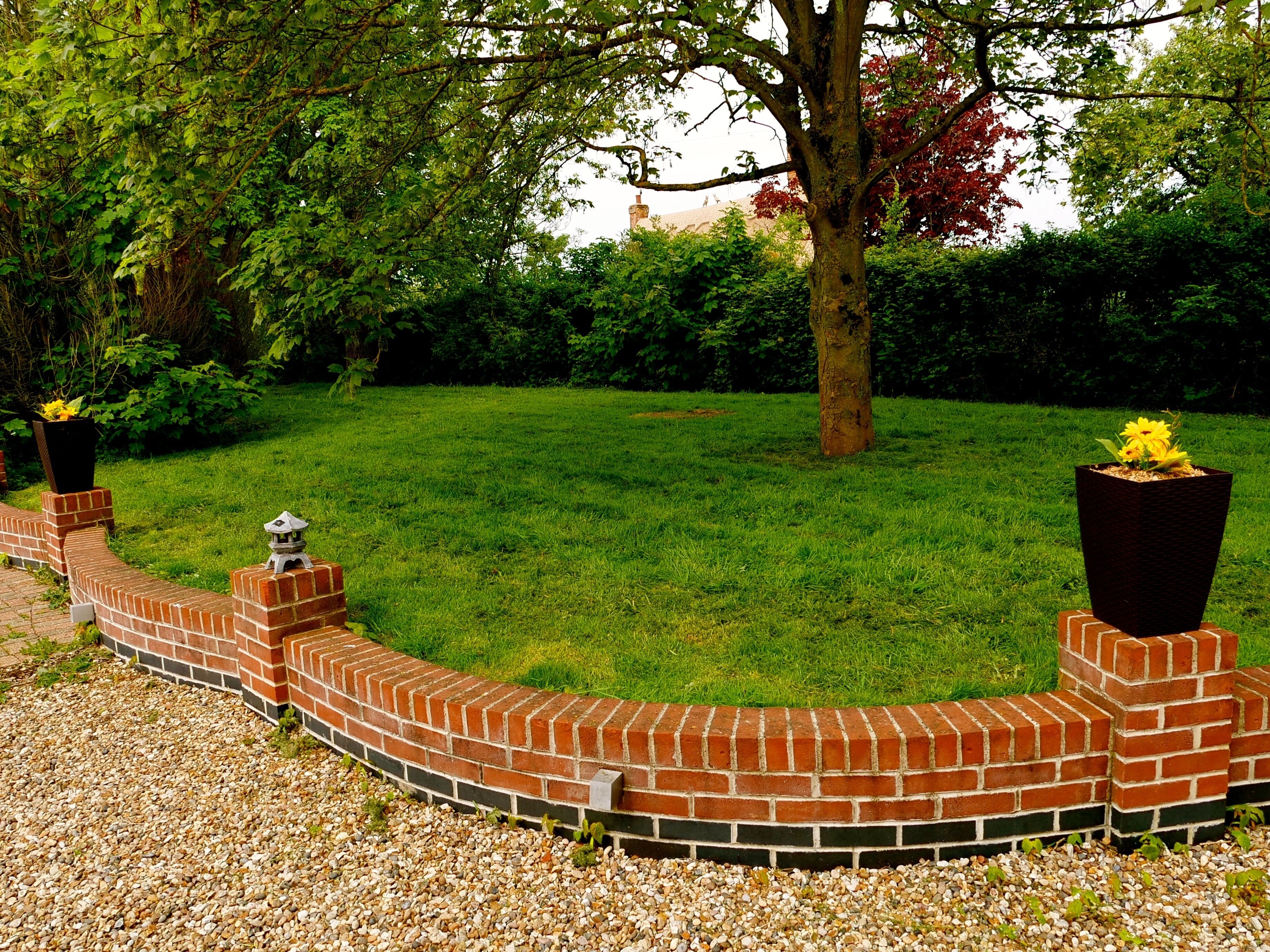 A brick garden wall with a curved design, surrounded by a grassy lawn and trees.