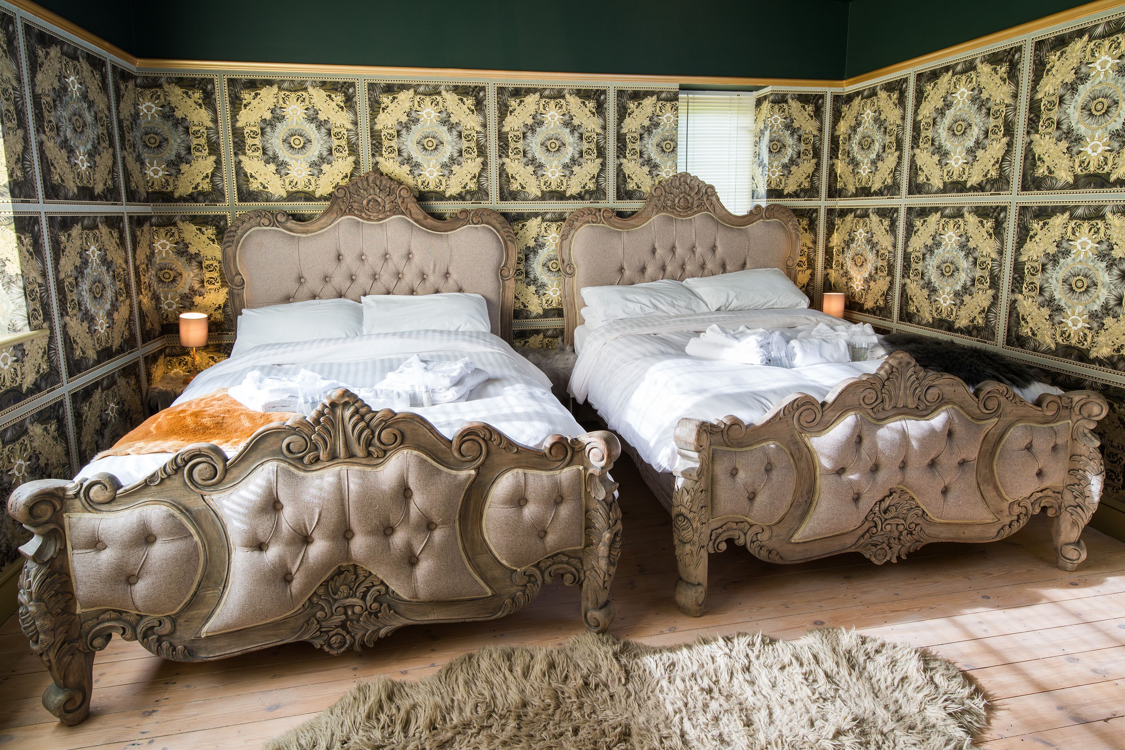 Une chambre dotée de deux lits richement décorés, d’un tapis moelleux et d’un papier peint à motifs.