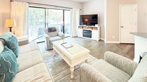 Una sala de estar con sofá, sillón, mesa de centro, televisor, chimenea y ventilador de techo.
