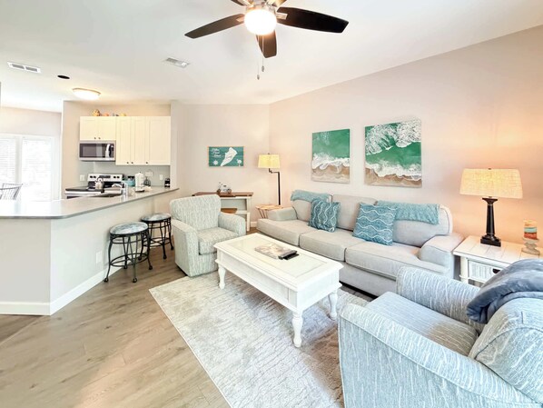 A modern living room with a sofa, coffee table, and a dining area with a kitchen in the background.
