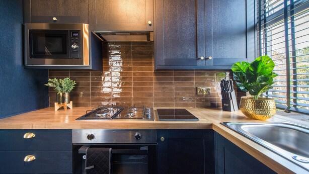 A modern kitchen with dark cabinetry, a stainless steel microwave, a gas stove, and a sink. - Luxury Versace 2 Bed, Hot Tub, Pool Table, Sky Tv (London)