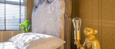 Un lit avec une literie blanche, une tête de lit décorative et une statue dorée représentant une figure assise tenant une lampe.