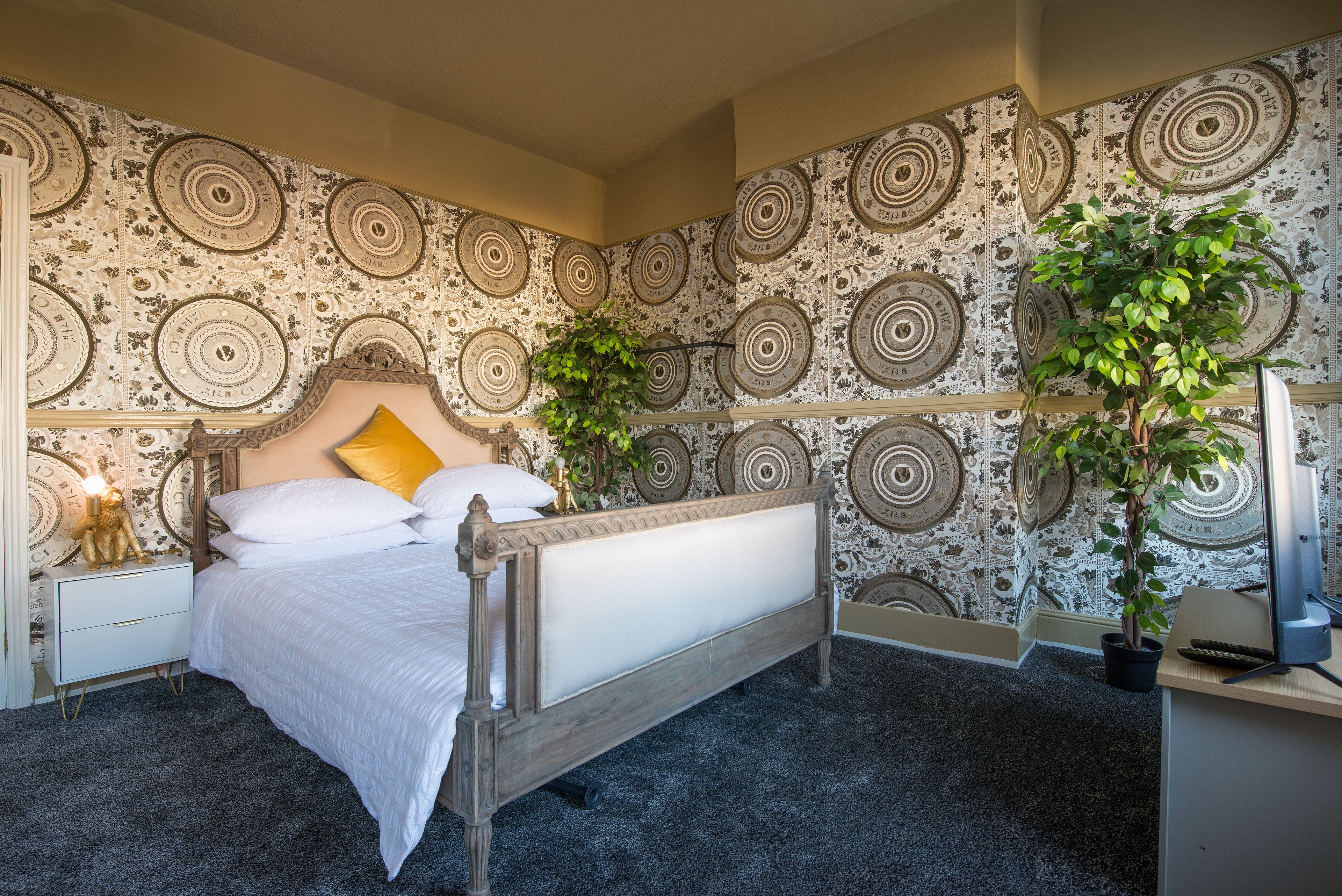 Een slaapkamer met een bed, een nachtkastje, een bureau en twee potplanten.