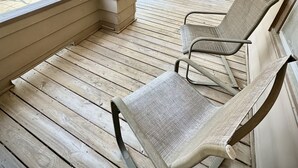 A covered porch with wooden flooring, two cushioned chairs, and a hanging planter.