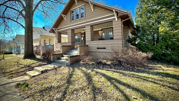 A two-story house with a front porch, a visible front door, and a staircase leading to the entrance.