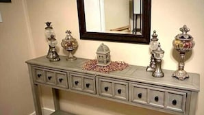 A grey console table with six drawers, a small decorative house, and various silver vases and candle holders.