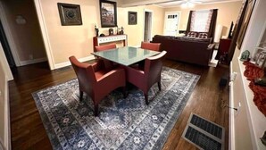 A dining area with a glass table and red chairs, a patterned rug, and a sofa in the background.