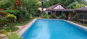 Relax by the serene pool surrounded by lush tropical vegetation and a guest house.