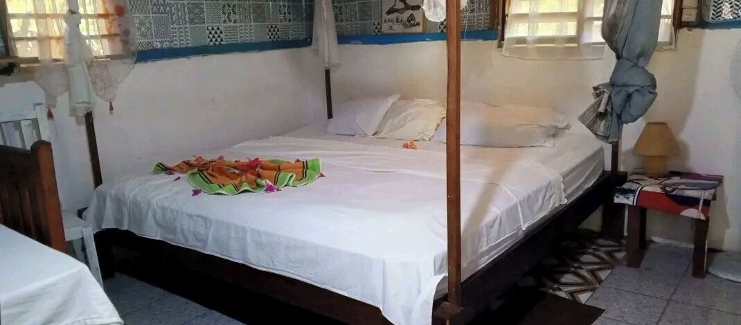 A single bed with a white sheet and a colorful blanket, a wooden headboard, and a small bedside table with a lamp.
