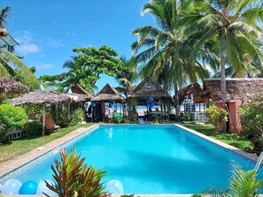 Relax by the serene pool surrounded by lush greenery and palm trees.