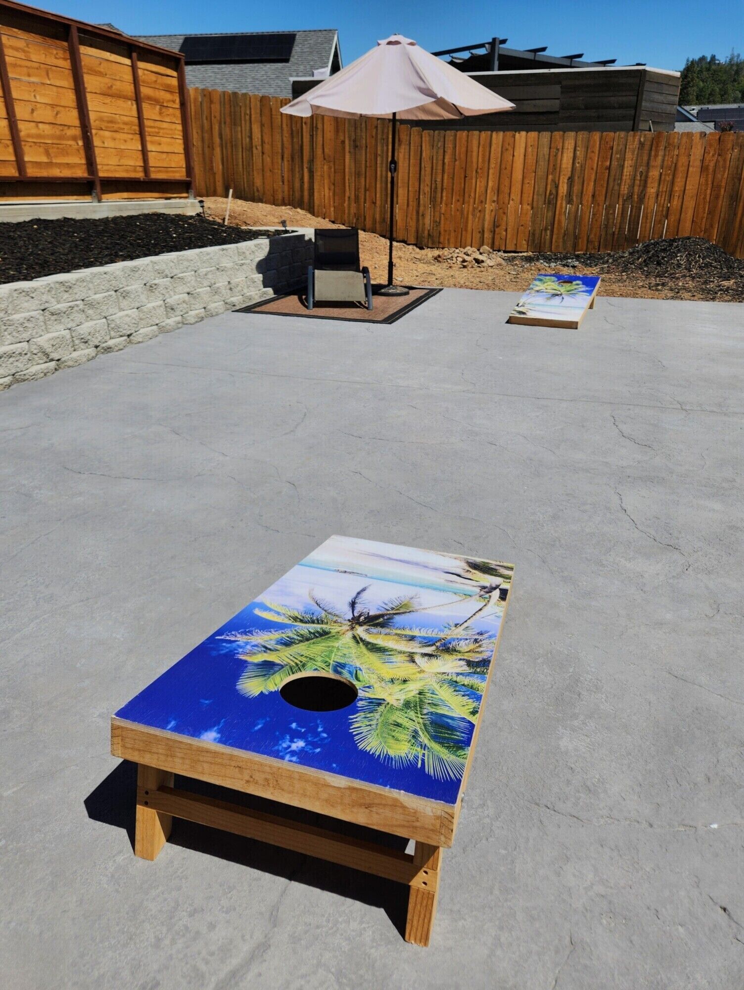 Een betonnen terras met een houten tafel, versierd met een tropisch palm ontwerp.