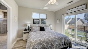 Une chambre à coucher comprenant un lit, des tables de chevet, un ventilateur de plafond et une grande fenêtre donnant sur le jardin.