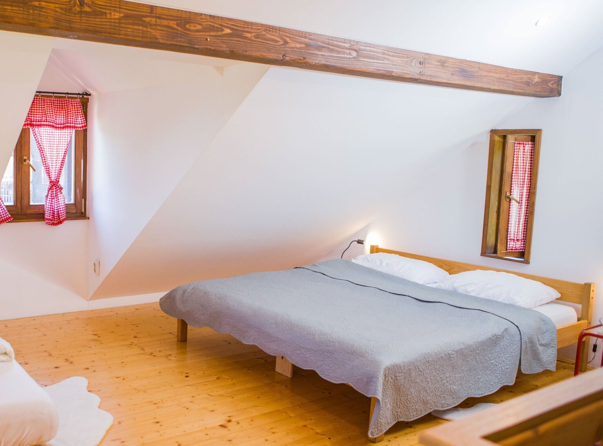 A bedroom with a sloped ceiling, a wooden bed frame, a grey bedspread, and a small bedside table.