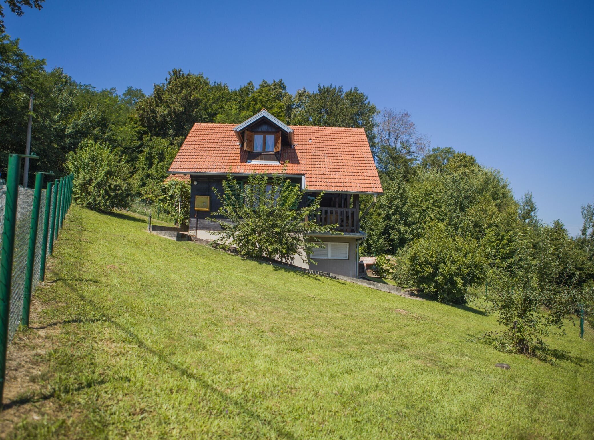 A house with a red-tiled roof, a balcony, and a grassy hill.
