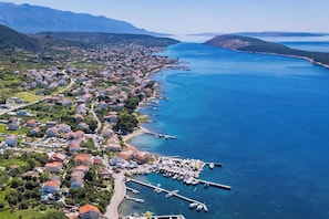 An aerial view of a coastal town with residential buildings, a marina, and a clear blue sea.