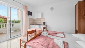 Une chambre d’hôtel avec deux lits, une petite kitchenette, un téléviseur fixé au mur et une porte-fenêtre coulissante donnant sur un balcon.