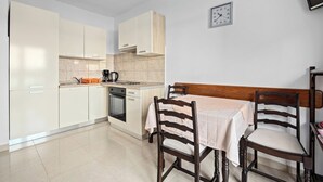 A compact kitchen with white cabinets, a wooden table, and two chairs. A clock is mounted on the wall. - Spectacular Sea View, Mooring - Jurica (Petra) (Rab)