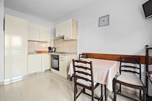 A compact kitchen with white cabinets, a wooden table, and two chairs. A clock is mounted on the wall. - Spectacular Sea View, Mooring - Jurica (Petra) (Rab)