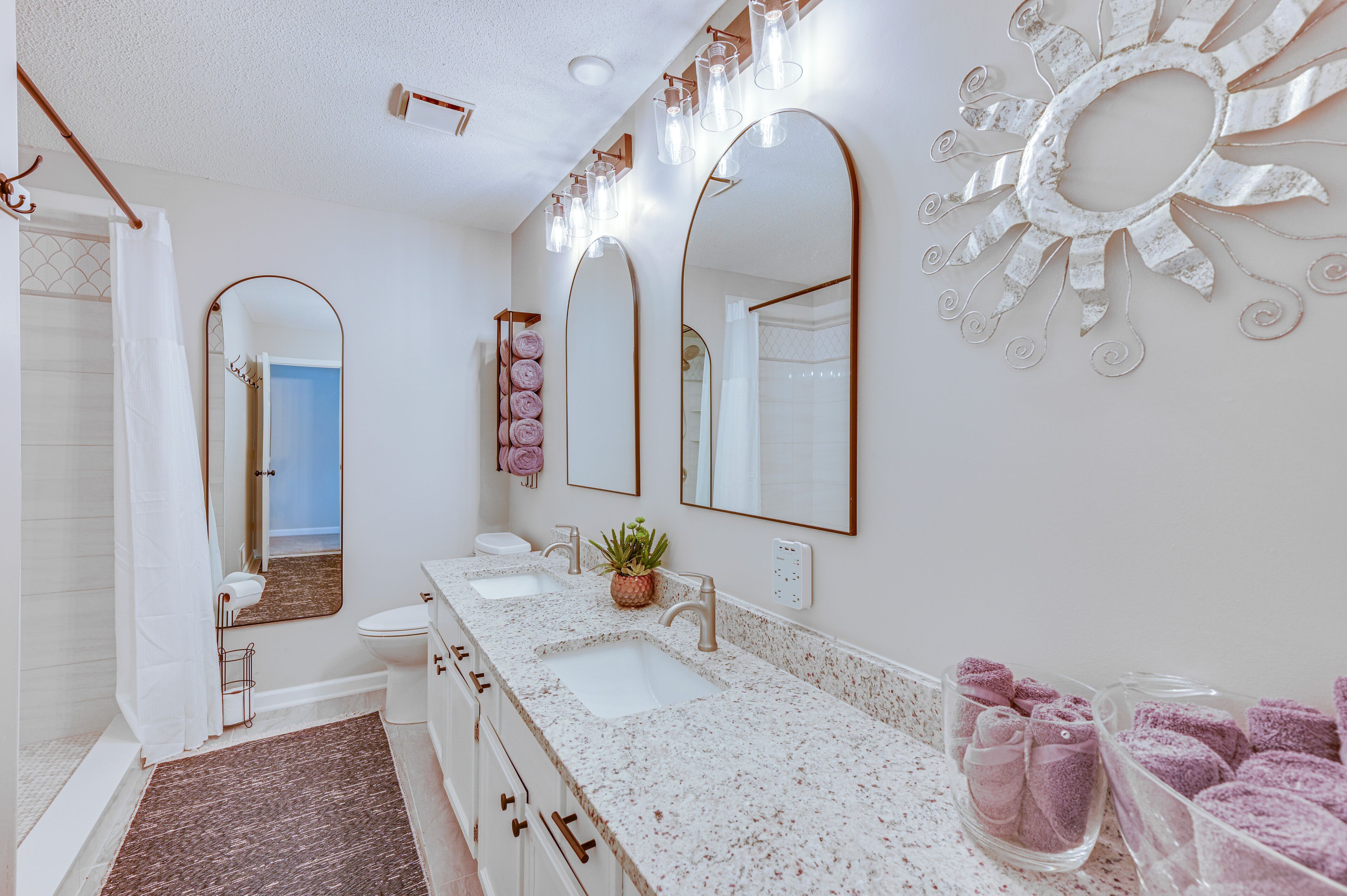 Un baño con lavamanos doble, un espejo grande y un adorno de pared con forma de sol.