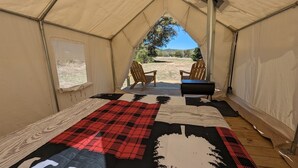A tent with a quilted floor, two wooden chairs, a grill, and a view of a grassy area with trees and hills. - Glamping Tents 1, 2, 3 (Vanderpool)
