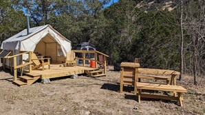A rustic wooden cabin with a porch, a small deck, and a table and bench set up for outdoor dining. - Glamping Tents 1, 2, 3 (Vanderpool)