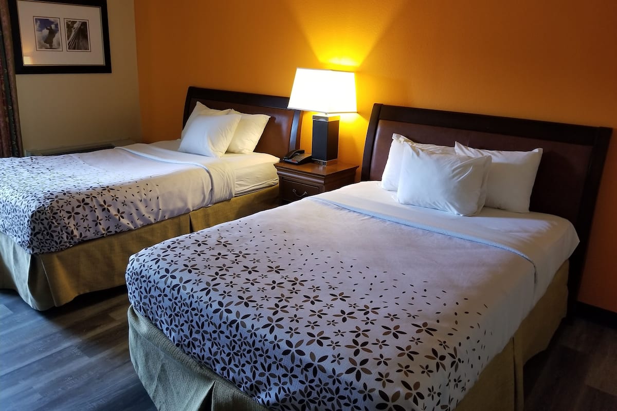 A hotel room with two beds, each with white linens and floral-patterned bedspreads. There is a nightstand with a lamp between the beds.