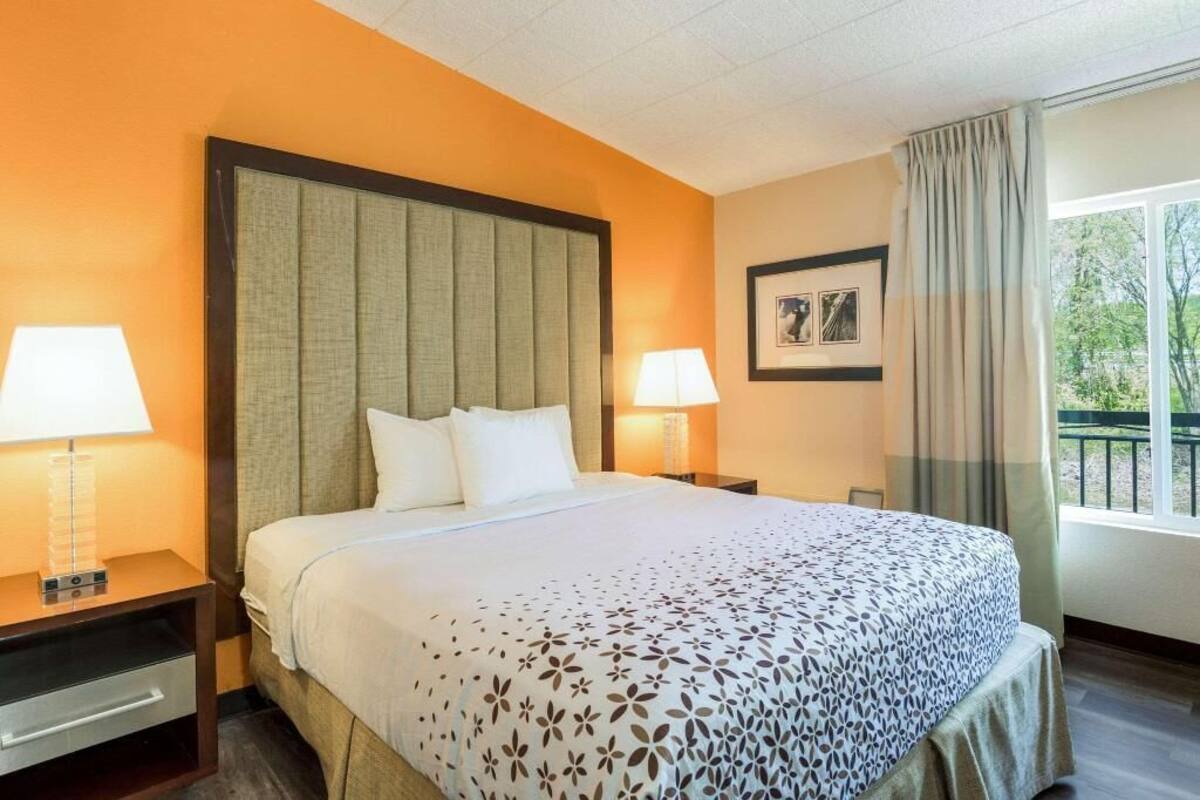 A hotel room with a large bed, two bedside tables with lamps, a framed picture on the wall, and a window with curtains.