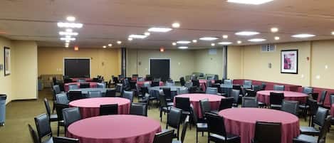A conference room with multiple round tables covered with red tablecloths, arranged in rows.