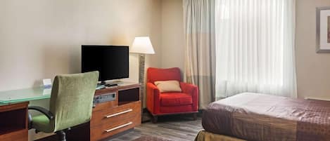 Ein Hotelzimmer mit Schreibtisch, Fernseher, rotem Sessel, zwei Betten und einem Fenster mit Vorhängen.