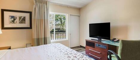 Quarto de hotel com cama, televisão sobre um móvel de madeira, uma cadeira e uma janela com cortinas.