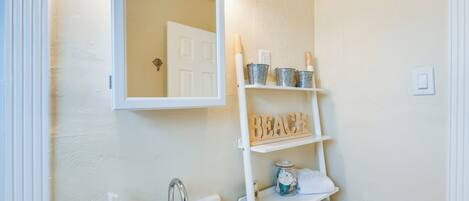 A bathroom with a white sink, a mirror above it, and a shelf with a 'BEACH' sign.