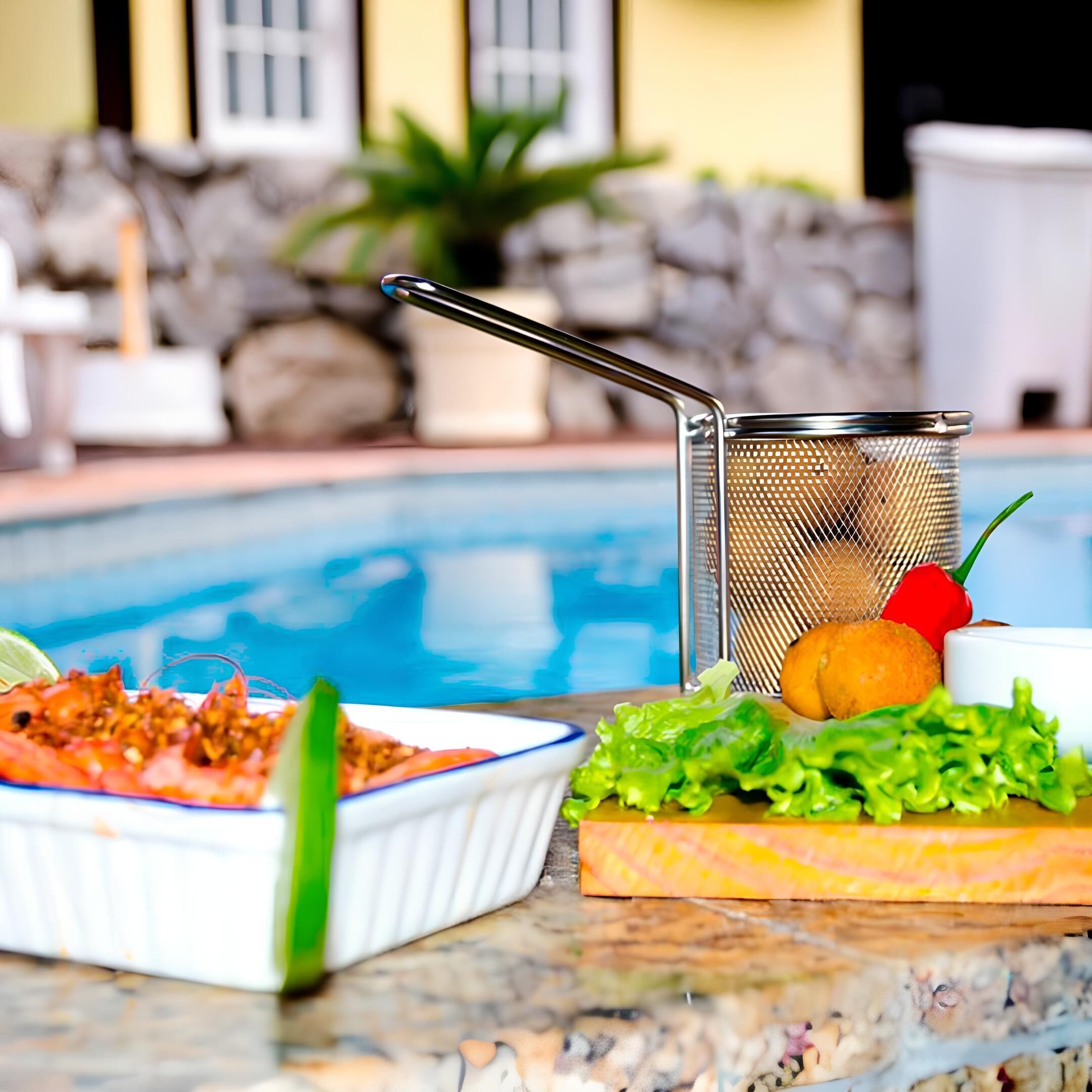 Ein Essbereich am Pool mit einem Metallsieb, einer Schüssel mit Essen und einem Teller mit Gemüse.