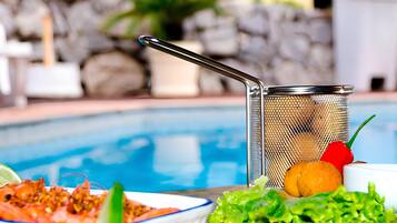 Mobiliario de comedor junto a la piscina, con un colador de metal, un cuenco de comida y un plato de verduras.