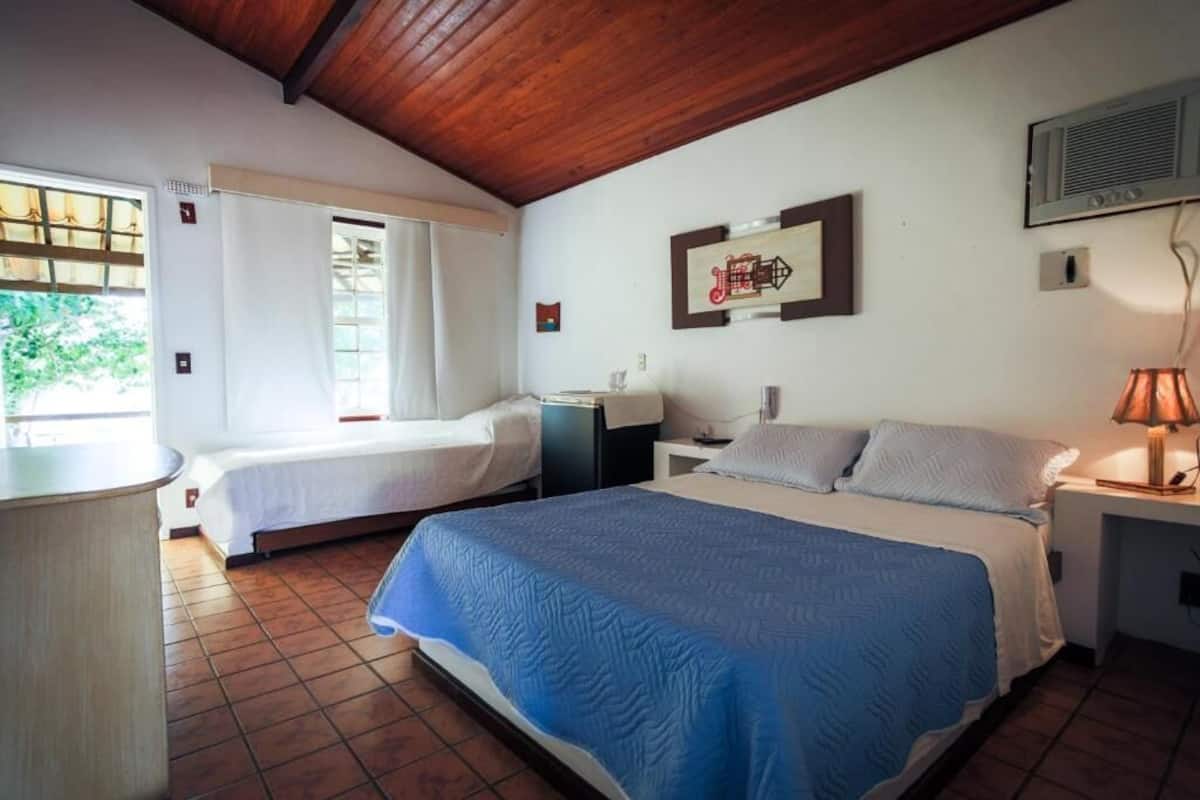 Habitación de hotel con dos camas, un escritorio, una silla, una lámpara y una ventana con cortinas.