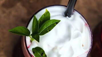 A glass of a creamy beverage with a black straw, garnished with green leaves, on a textured surface.