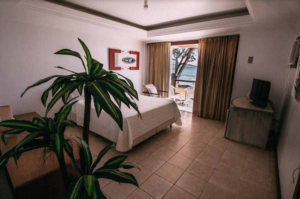 A hotel room with a bed, a desk, a chair, a television, and a view of the ocean through a window.