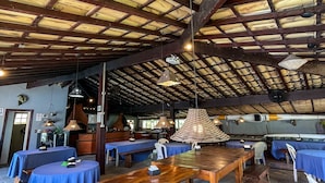 Um espaço interno amplo, com pé direito alto, mesas e bancos de madeira e toalhas de mesa azuis.