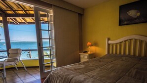Quarto de hotel com cama, uma cadeira, mesa de cabeceira, luminária e vista para o mar.