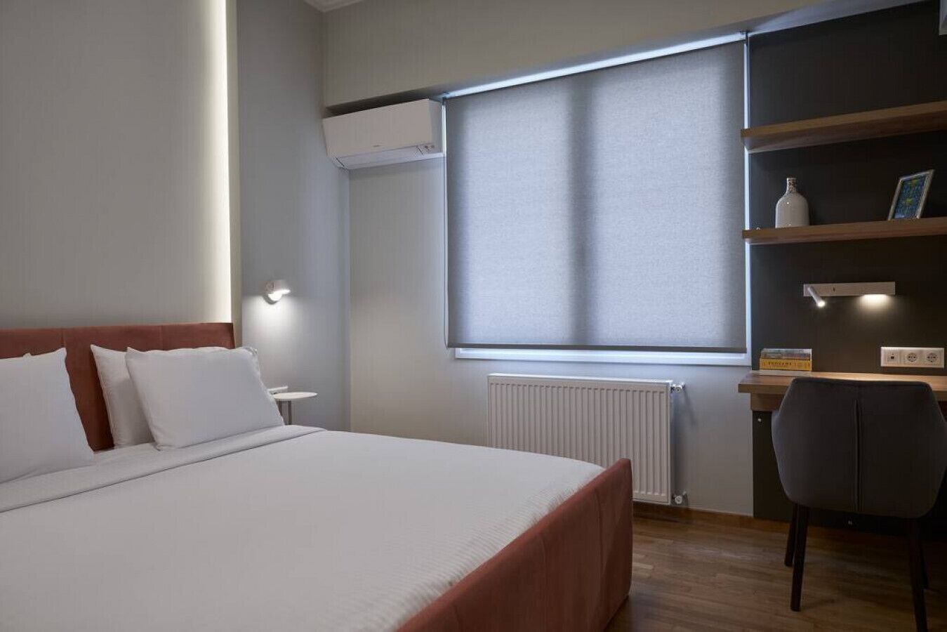 Une chambre d’hôtel moderne, dotée d’un grand lit, d’un bureau avec une chaise, d’un radiateur et d’une fenêtre avec des stores.
