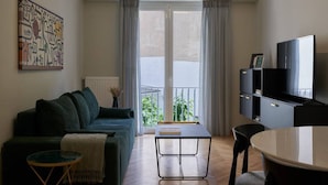 A modern living room with a sofa, a coffee table, a TV, and a balcony with curtains. - Little Gem: Modern Urban Retreat (Athina)