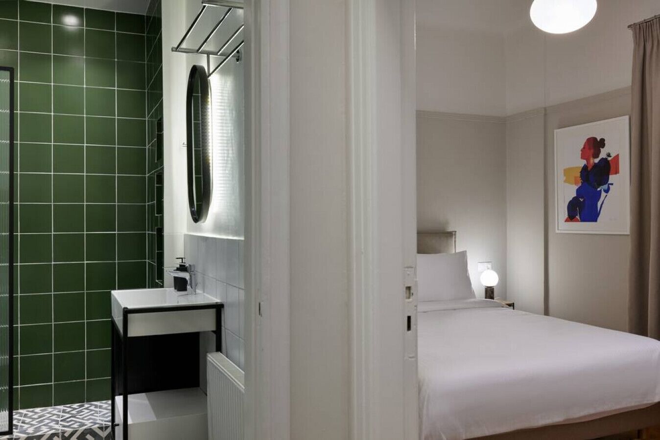 Et hotelværelse med en seng, et natbord, et spejl og en væg med grønne fliser.