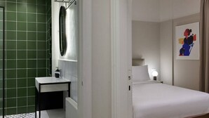 Una habitación de hotel con una cama, una mesita de noche, un espejo y un muro con azulejos verdes.